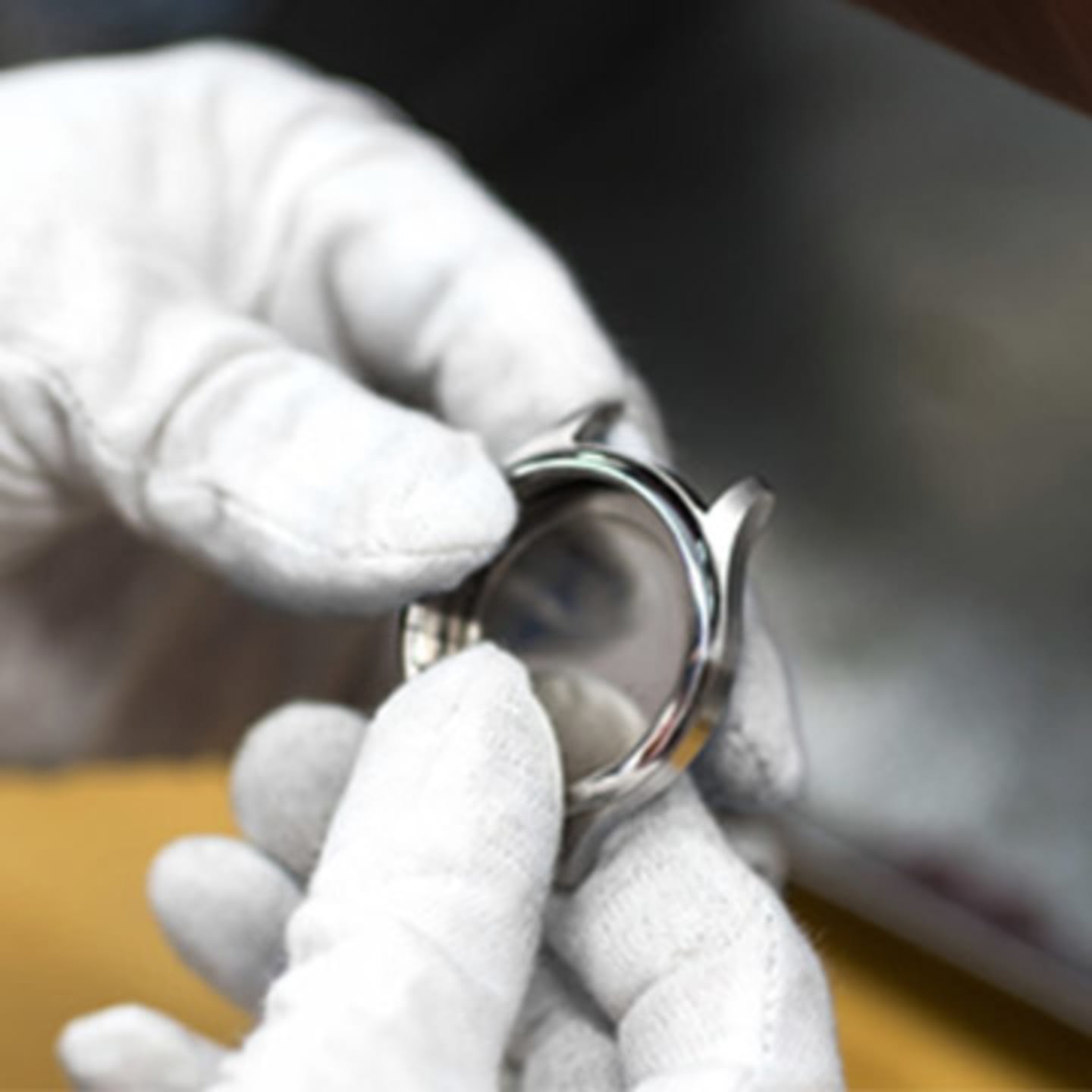 Watch maker with white gloves holding a silver watch body in their hands